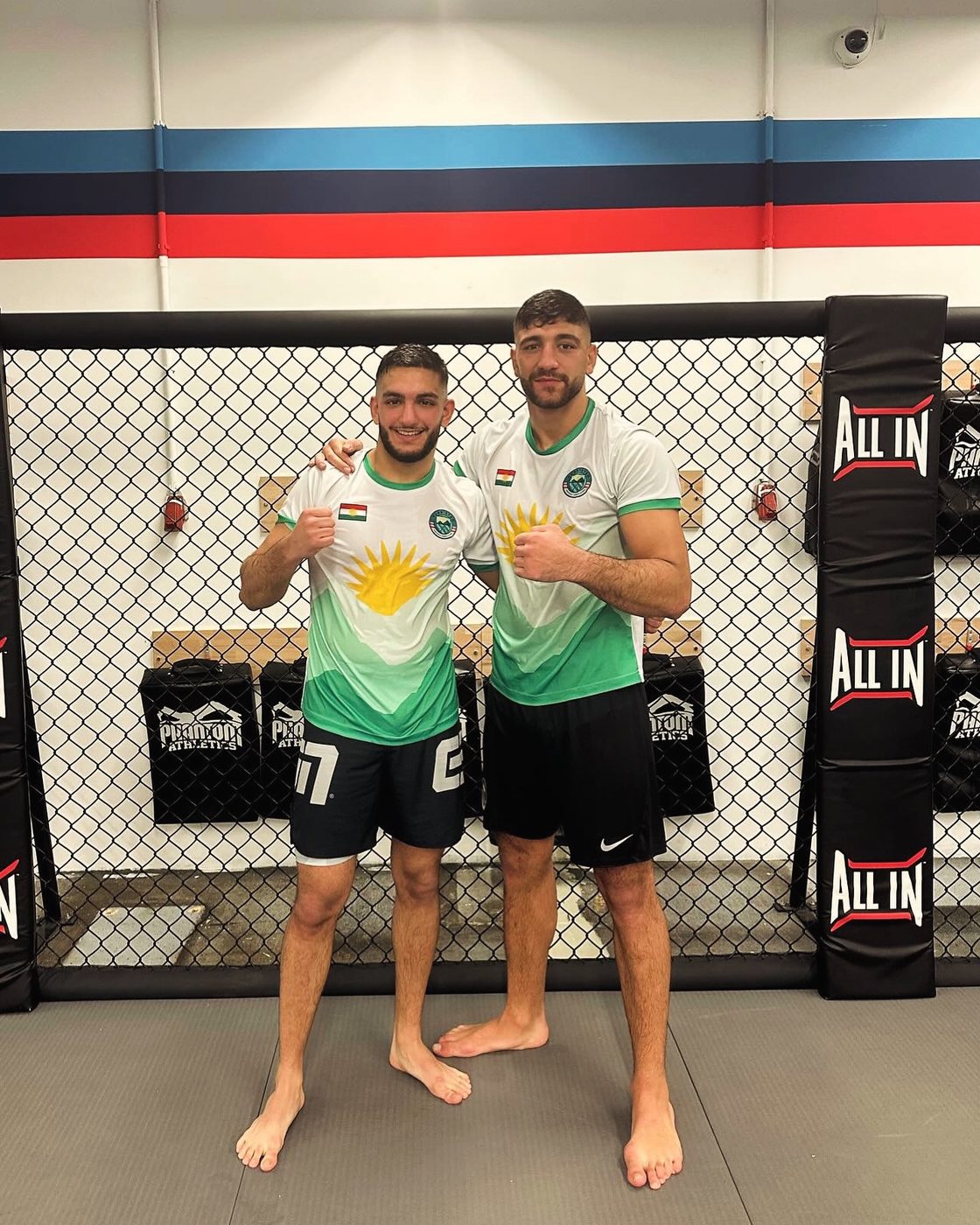 Two Kurdish MMA fighters in Çiyayê Kurdî shirts in front of the cage