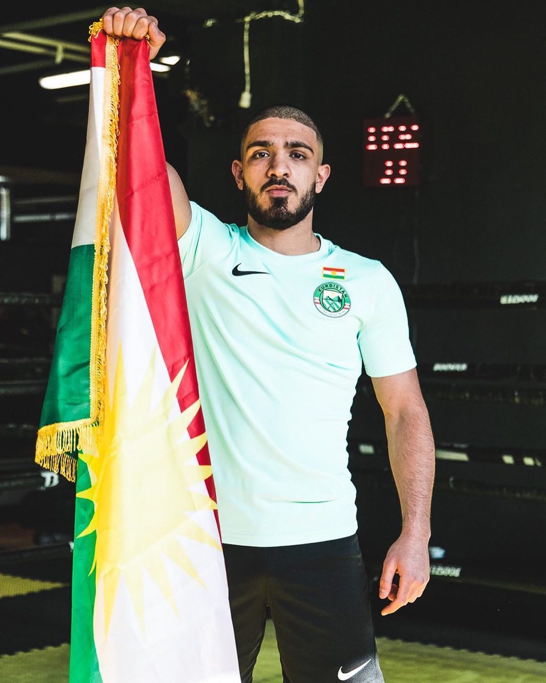 Kurdish MMA fighter holding the flag of Kurdistan in the training gym