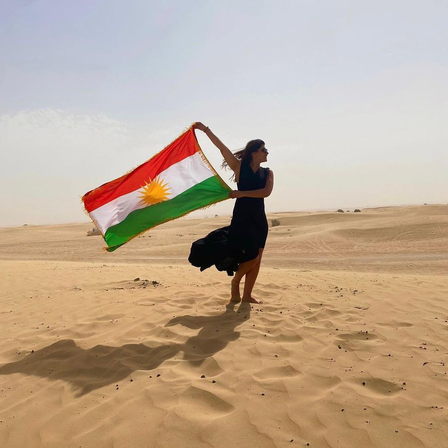 Kurdish woman carrying the flag of Kurdistan in the desert