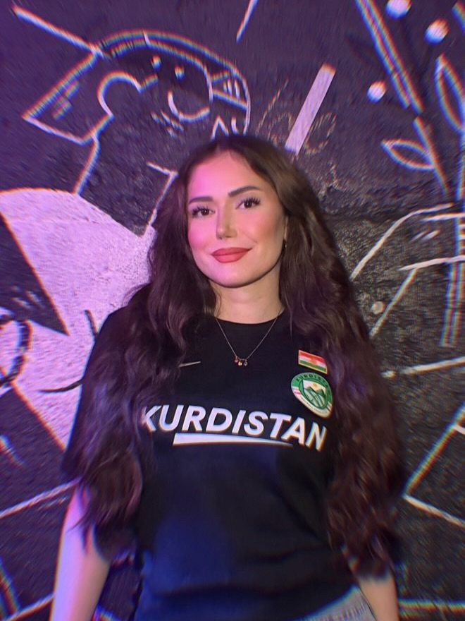 Young Kurdish woman in a black Kurdistan Nike shirt in front of a mural